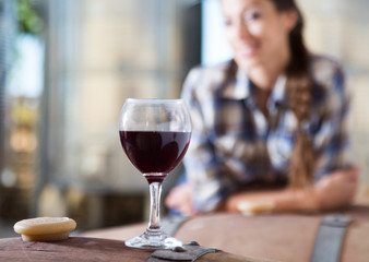 girl looking at glass of red wine standing on wooden barrel in winery