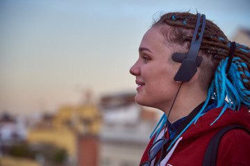 A young girl with blue dreadlocks listening to music in the city.