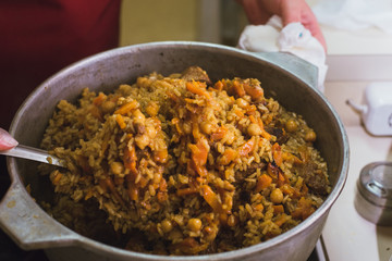 Cooking oriental pilaf in the kitchen in the cauldron. A woman prepares a dish of lamb, beef, rice, chickpeas, carrots