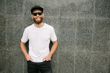 Hipster handsome male model with beard wearing white blank t-shirt and a baseball cap with space...