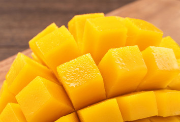 Fresh chopped mango cubes on wooden cutting board and rustic timber background. Tropical summer fruit concept, close up, macro, copy space.