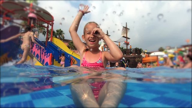 Happy girl playing in outdoor swimming pool on summer vacation on tropical beach.