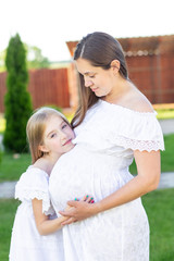 Pregnant mom and daughter are resting in nature. Long-haired girls in white dresses. Pregnant girl with long hair