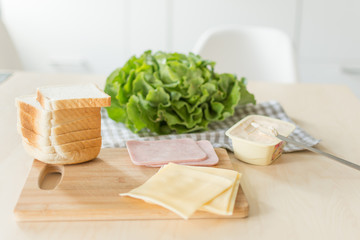 Composition for making sandwich with cheese and ham on a wooden table in the bright kitchen. Lunch. Sandwich with lettuce. Healthy eating concept.
