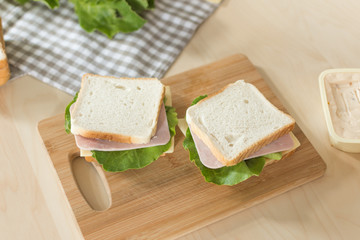 Sandwich with cheese and ham on cutting board on the table in the bright kitchen. Lunch. Sandwich with lettuce. Healthy eating concept.