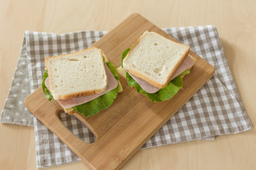 Sandwich with cheese and ham on cutting board on the table in the bright kitchen. Lunch. Sandwich with lettuce. Healthy eating concept.