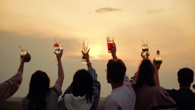 Cheerful company meets sunset on the Rooftop of the house, raised his hands with summer urban cocktails up
