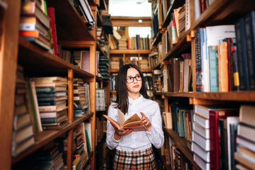 people, knowledge, education and school concept - happy student girl or young woman with book posing in an old library