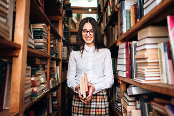 people, knowledge, education and school concept - happy student girl or young woman with book posing in an old library