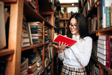 people, knowledge, education and school concept - happy student girl or young woman with book posing in an old library