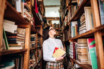 people, knowledge, education and school concept - student girl select a book on the shelf in the old library