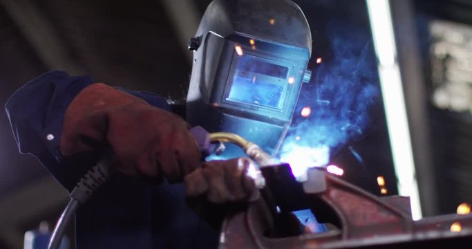 4K Female welder in metal workshop lifting up visor & smiling. Slow motion.
