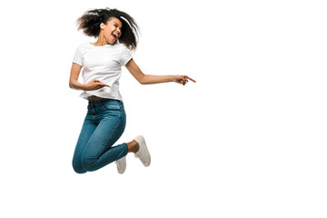 smiling african american woman pointing with fingers and jumping isolated on white