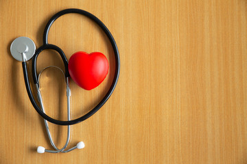Black doctor stethoscope and stress ball in heart shape on wooden floor background. Medical healthcare concept.