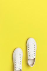 White female fashion sneakers on yellow background. Flat lay top view copy space. Women's shoes. Stylish white sneakers. Fashion blog or magazine concept. Minimalistic shoe background, sport