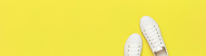 White female fashion sneakers on yellow background. Flat lay top view copy space. Women's shoes. Stylish white sneakers. Fashion blog or magazine concept. Minimalistic shoe background long banner