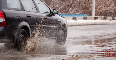 The car b stro drives through a puddle of dirt, sprays fly from under the wheels