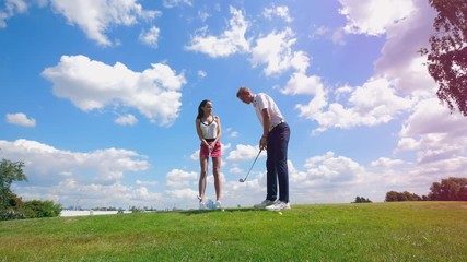 Man and woman training with clubs at a golf filed.