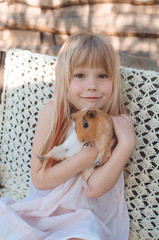 White girl blonde with a pet in her arms. Cute caucasian child of  with a guinea pig in her arms. Bright summer composition