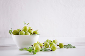 Bowl full of ripe fresh gooseberries on the white table against white background