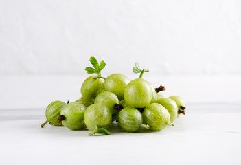 Heap of fresh gooseberries with green leaves on the white surface