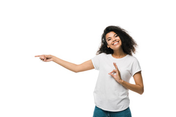 happy african american woman pointing with finger while showing ok sign isolated on white