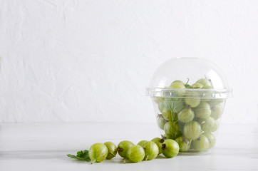 Plastic cup of juicy gooseberries on the white surface.Empty space for text