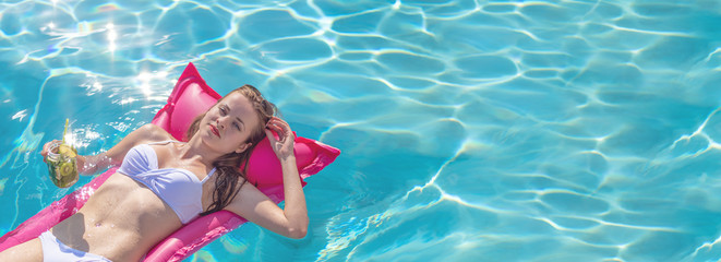 Summertime in pool. Young and beautiful woman floating on inflatable mattress in pool with green cocktail.