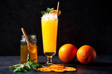 Delicious cocktail paired with jar of honey, green leaves and two oranges