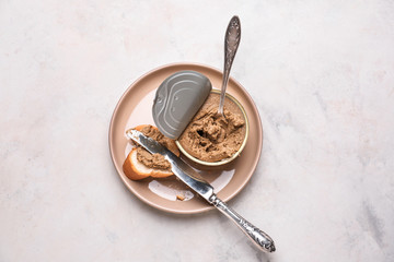 Plate with slice of bread and meat pate in tin can on light table