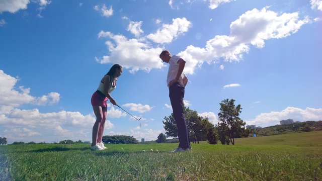 A woman hits a ball while a man watching on a golf field.
