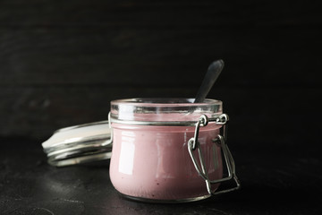 Glass jar with fruit yogurt on black cement background, space for text