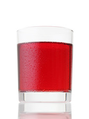 Glass of red drink covered by water drops on white
