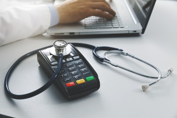 medical costs and health care expenses concept - payment terminal with stethoscope on the table in...