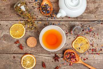 cups of healthy herbal tea with cinnamon, dried rose and camomile flowers in spoons over wooden...