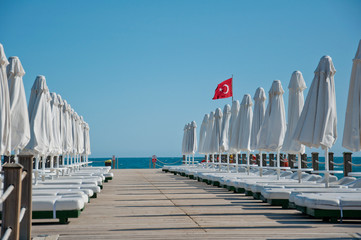 A wooden pier with the turkish flag, white chairs and beach umbrellas. Destination Turkey. Travel...