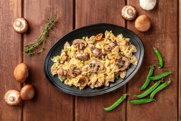 Mushroom and cheese pasta. Farfalle with cremini and green peas, shot from the top with ingredients on a dark rustic wooden background