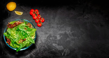Fresh green salad with spinach, arugula, romaine and lettuce in a glass bowl on dark background. Top view with copy space