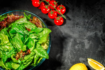 Fresh green salad with spinach, arugula, romaine and lettuce in a glass bowl on dark background. Top view