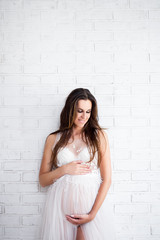 attractive pregnant woman in white lace dress over white brick wall with copy space