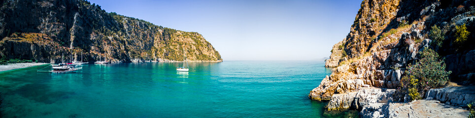 Secluded beach surrounded by valley cliffs in a tranquil bay with turquoise water and sailing boats at sunrise, Oludeniz, Turkey panoramic © Studio-FI