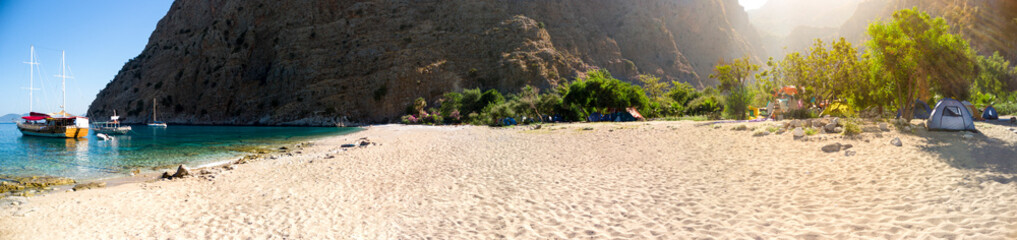 Camping on the beach in a secluded bay with turquoise water and sailing boat at sunrise, Oludeniz, Turkey panoramic