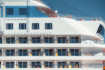 Side close-up view of the facade of a modern bright cruise ship with rows of cabin windows and balconies, upper deck, multiple portholes, glass fence, hammocks on several balconies; Lisbon, Portugal