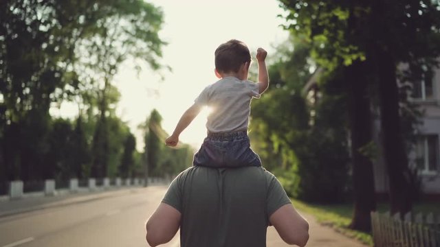 Father and son walking in city at sunset, Two year old kid is sitting on the parent's shoulders