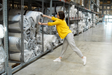 Girl with glasses takes a big and heavy mattress in the store. Wholesale and purchase. Self-service warehouse. Selection of products