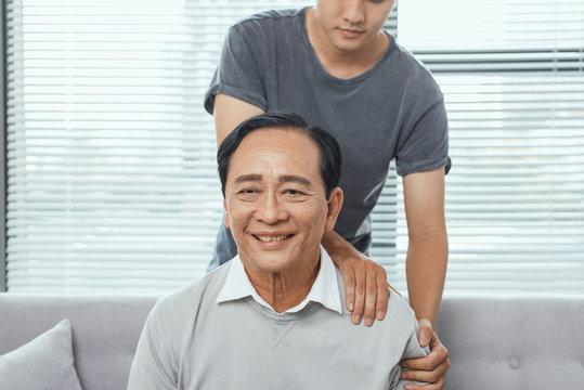 Asian Old Man Shoulder Pain, Sitting On Sofa , Son Massaging Father Shoulder.