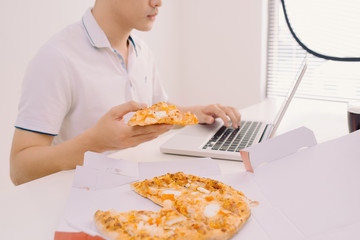 Male freelancer eating pizza while working  at home office