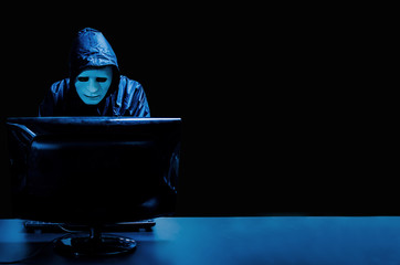Anonymous computer hacker in white mask and hoodie. Obscured dark face standing in the middle and...