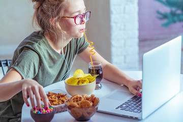 Girl works at a computer and eats fast food. Unhealthy food: chips, crackers, candy, waffles, cola....