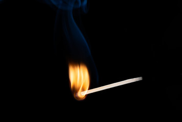 Burning wooden match with smoke over black background. Copy space